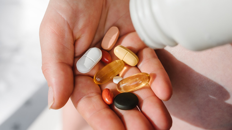 A hand holding a wide variety of vitamins and supplements