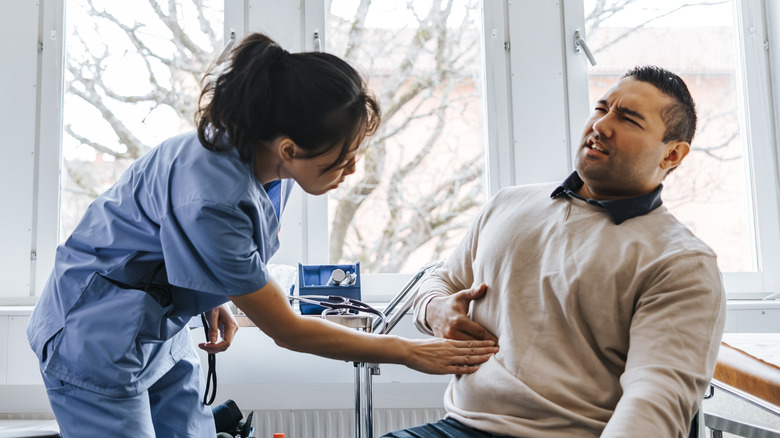 A man pointing to the upper right abdominal pain to his doctor