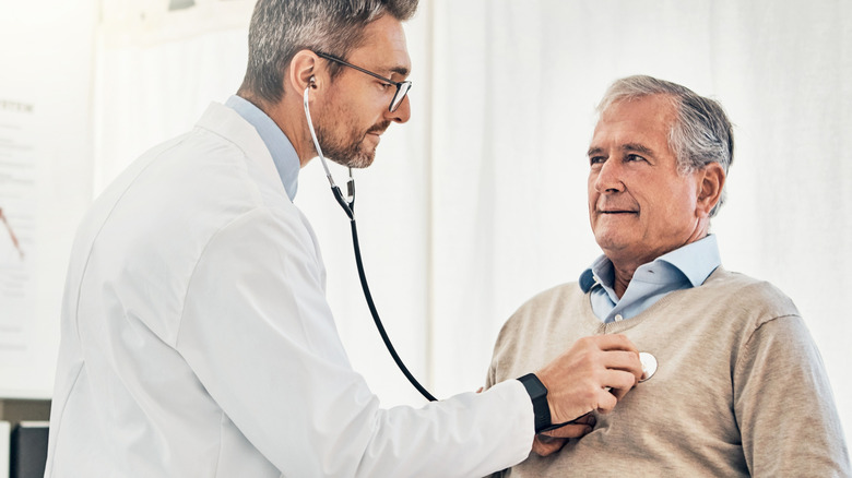 A doctor checking a man's heart with a stethoscope