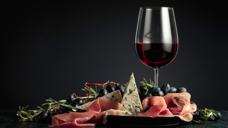 glass of red wine with grapes, prosciutto, and blue cheese