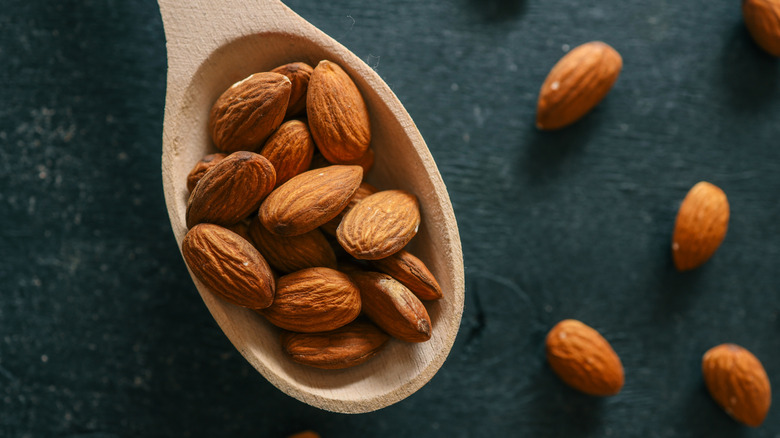 Wooden spoon filled with raw almonds on a rustic dark surface.