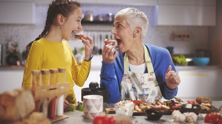 A happy child and a white-haired woman sampling food in the kitchen