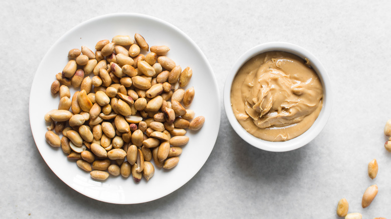 Top view of a plate of roasted peanuts and a bowl of creamy peanut butter