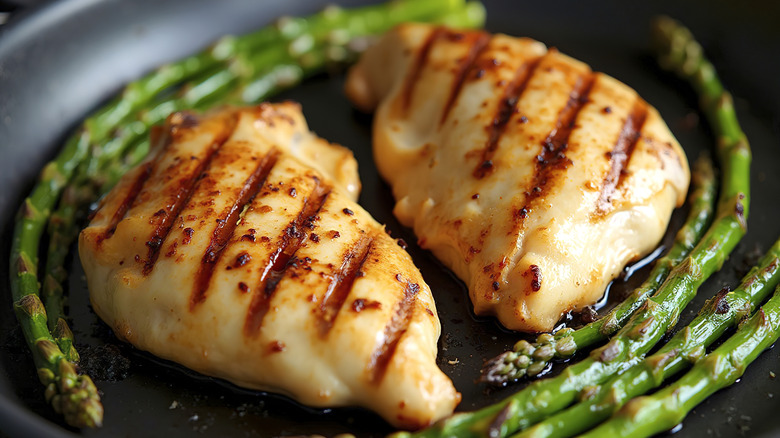 Two grilled chicken breasts on a grill pan with asparagus spears