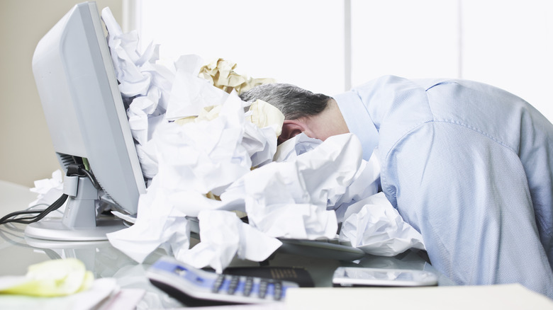 Man at office with face in piles of paperwork