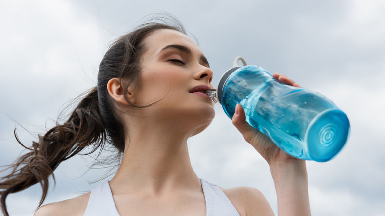 woman drinking water outside during workout