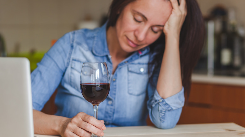 Woman holding her head while drinking wine