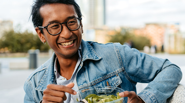 Smiling man eating salad outdoors