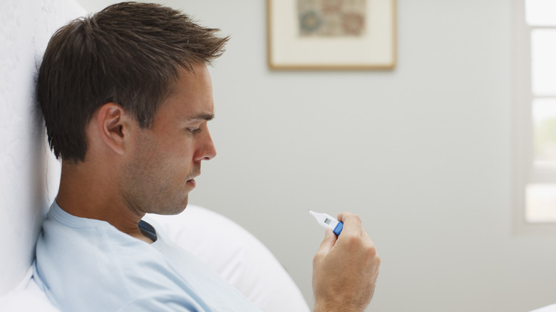 Man in bed checking his temperature