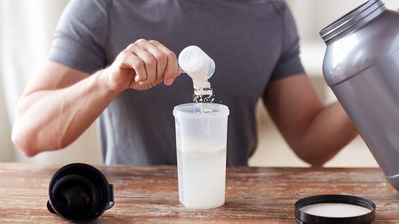 A fit man adding a scoop of creatine to a shaker cup