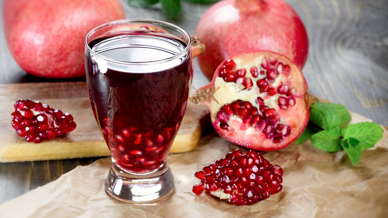 A glass of pomegranate juice sitting on a table surrounded by pomegranates