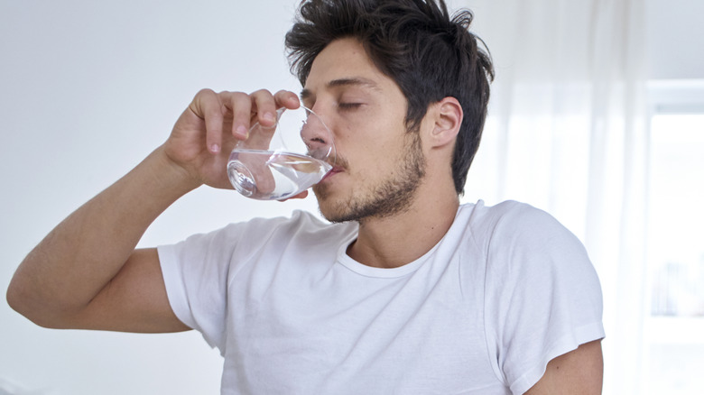 A man sitting in bed drinking a glass of water