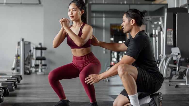 Trainer helping woman with squats