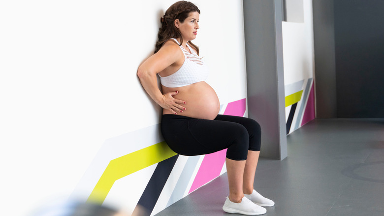 pregnant woman squatting against wall