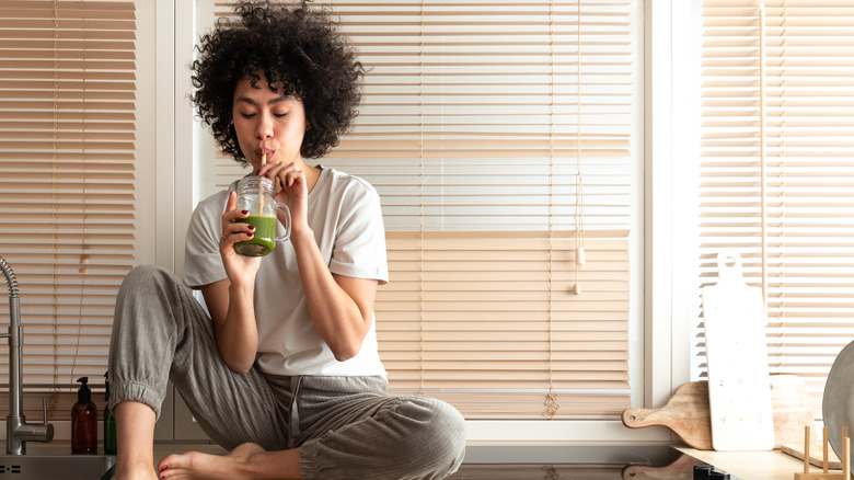 woman sitting on her kitchen counter drinking green juice