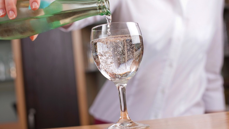 woman pouring seltzer water into wine glass