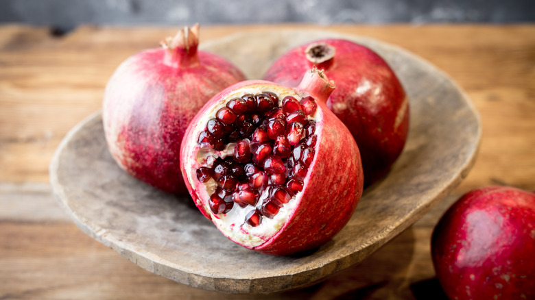 A pomegranate cut open to reveal its seeds surrounded by two other pomegranates