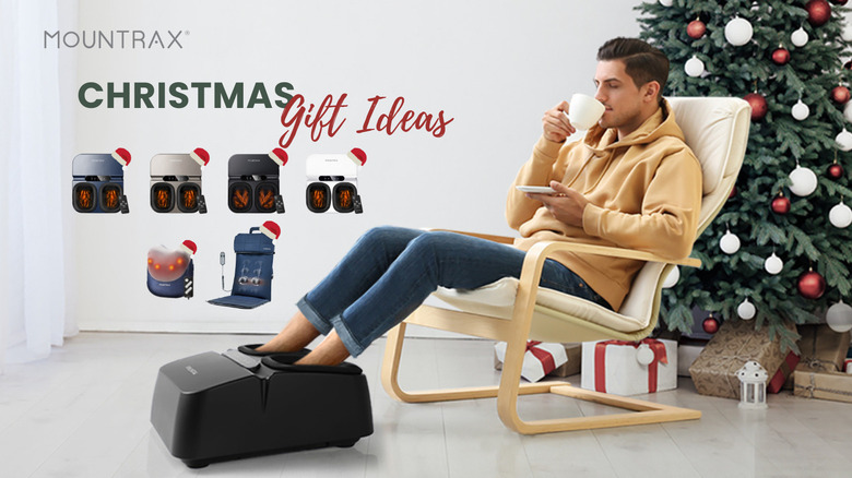 A man dipping his feet into a foot massager while sipping tea by a Christmas tree