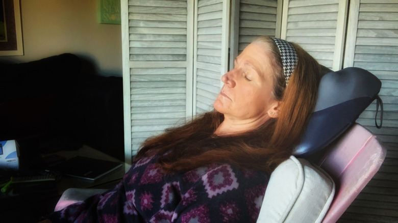 A woman using a neck massager while lying in a chair