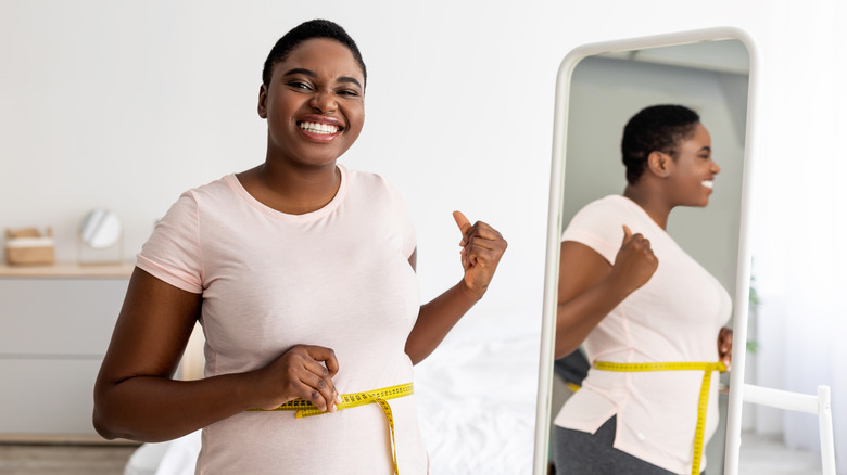 happy woman measuring her waist in front of mirror