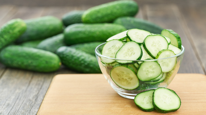 sliced cucumbers in a bowl with whole cucumbers in the background