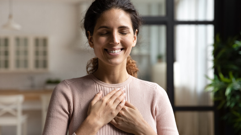 A woman smiles and looks happy with her hands over her heart