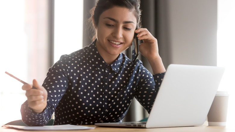 Smiling woman on phone with pen in hand and laptop open