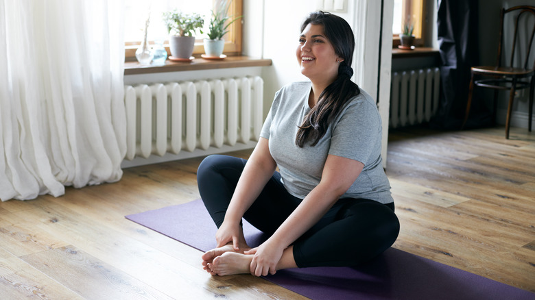 Woman sitting on mat with hands on bare feet, doing butterfly stretch