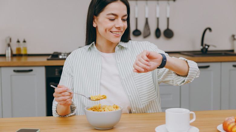 smile young woman looking at watch eating breakfast