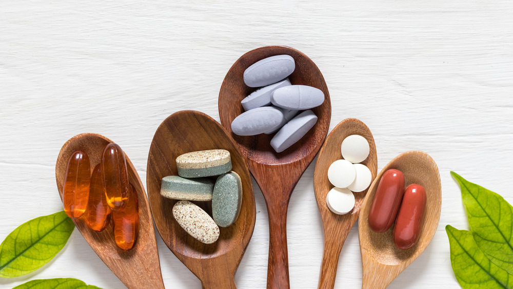 Vitamin pills arranged in wooden spoons with green leaves