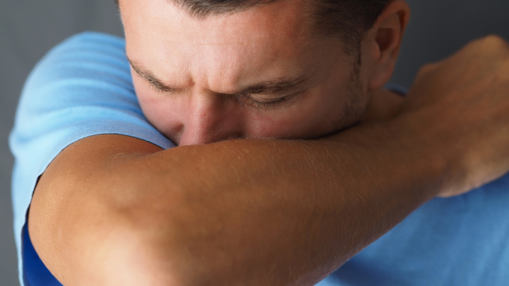 close up of man sneezing into his elbow