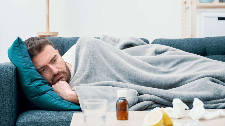 a man laying on his couch resting with medicine bottles and water on the coffee table 