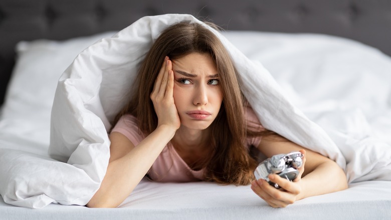 woman in bed holding alarm clock