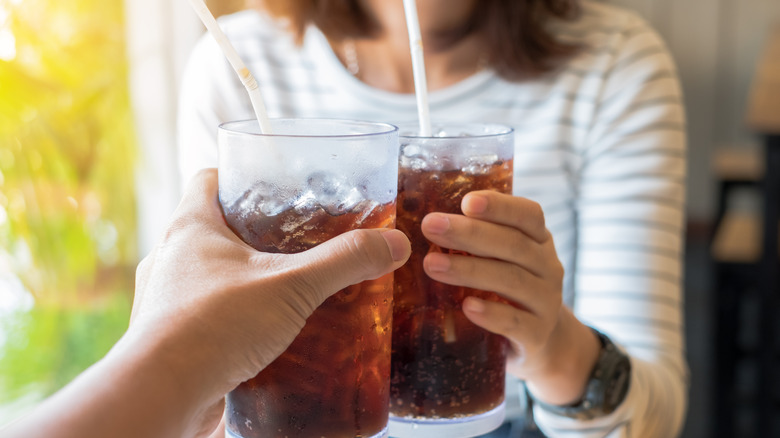 Two hands holding glasses of soda