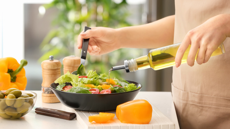 A woman dresses a salad with a bottle of oil