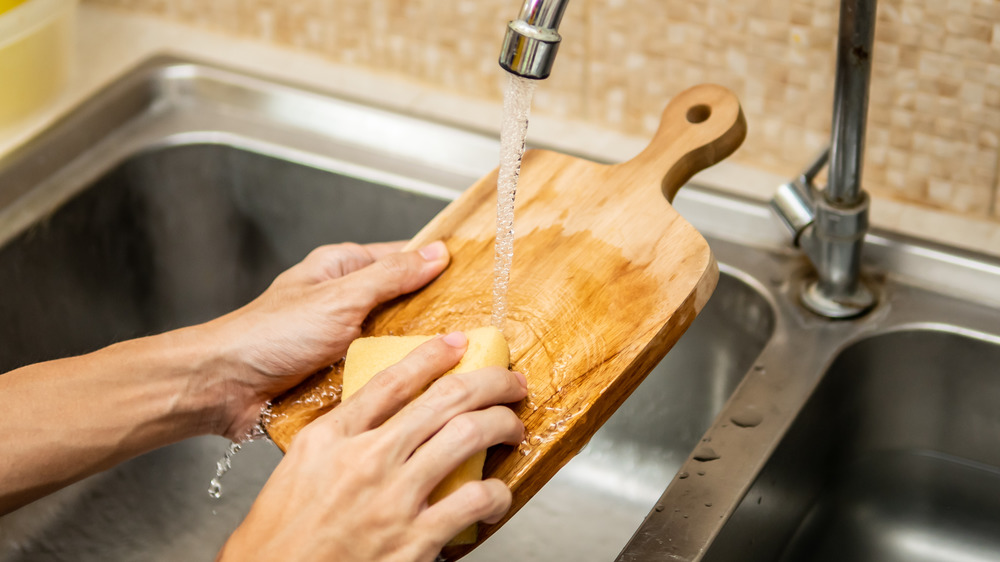 Close up of hands cleaning wooden chopping board in sink