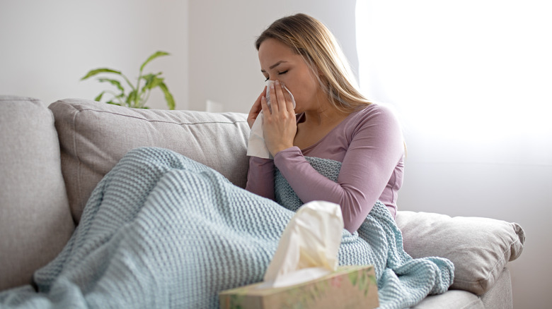 woman under blanket blowing nose in tissue