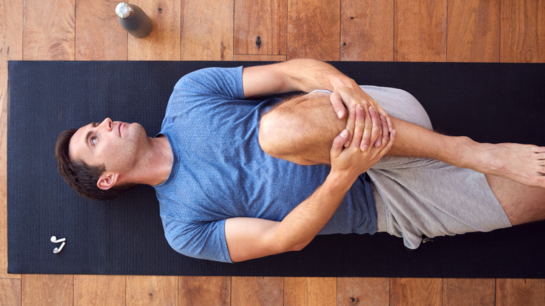 Man grasping leg on yoga mat