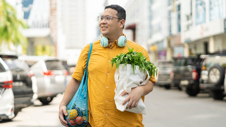 A man carrying vegetables, fruit, and other groceries in reusable bags