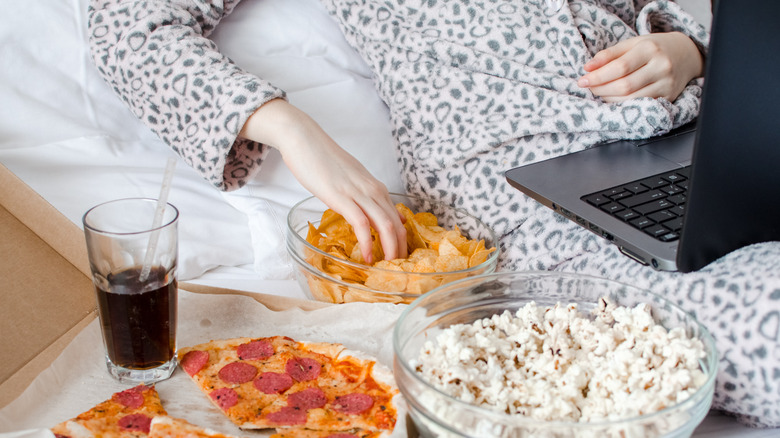 woman eating junk food in bed with computer
