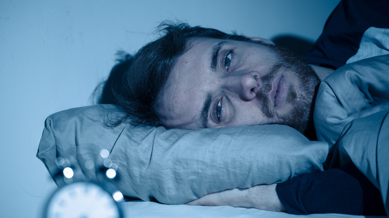 man looking worried in bed with alarm clock