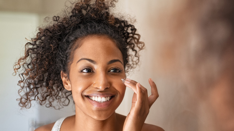 young woman happily applying skincare in mirror