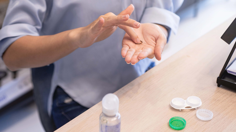 Person in a light blue shirt rubbing their contact lens in their hand