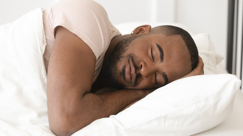 Man smiling as he peacefully sleeps in his bed on his side