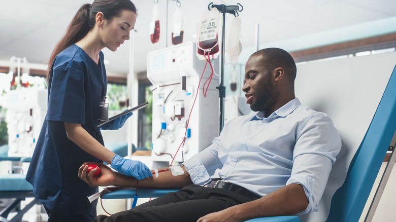 man giving blood in medical office being helped by tech