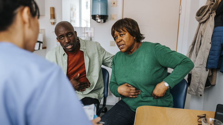 A woman holding her abdomen while sitting next to her son in a doctor's office