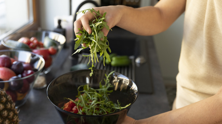 man adding arugula to salad while in kitchen at home