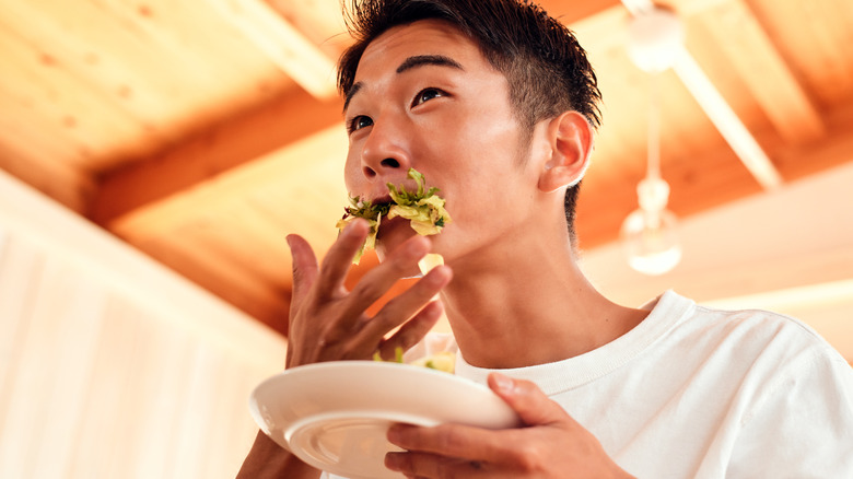 young man eating leafy greens from plate with hands