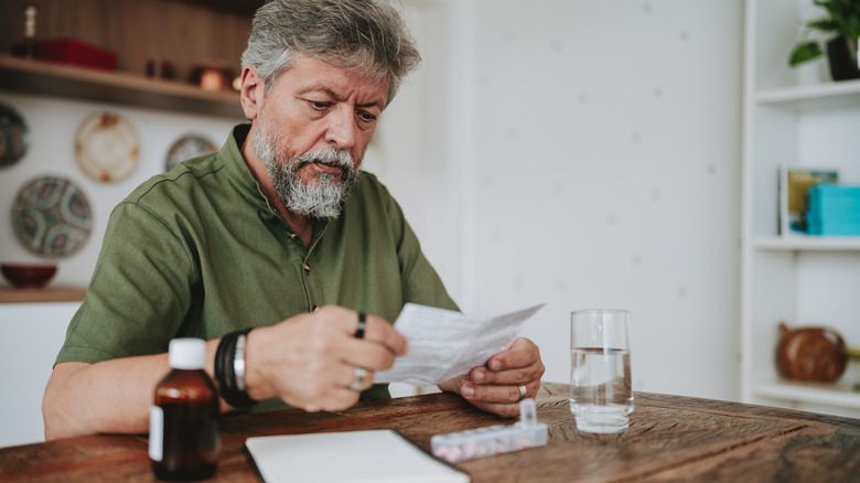 older man looking at pharmaceutical insert in kitchen