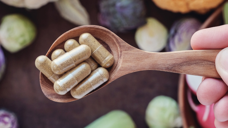 Hand holding wooden spoon with supplements 